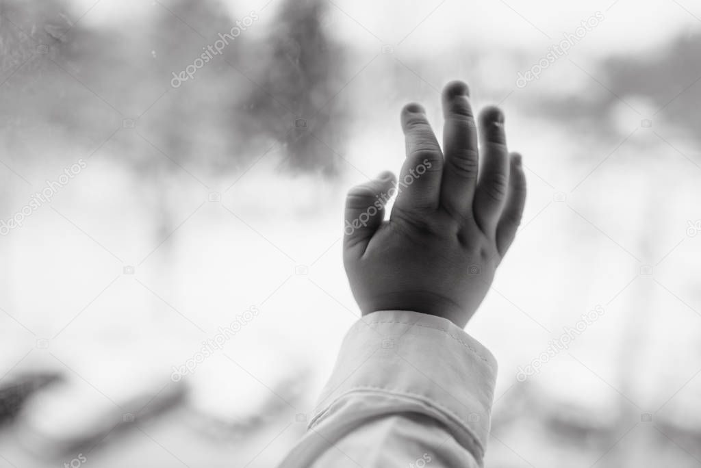 Young boy at window (in partial silhouette) hands pressed agains