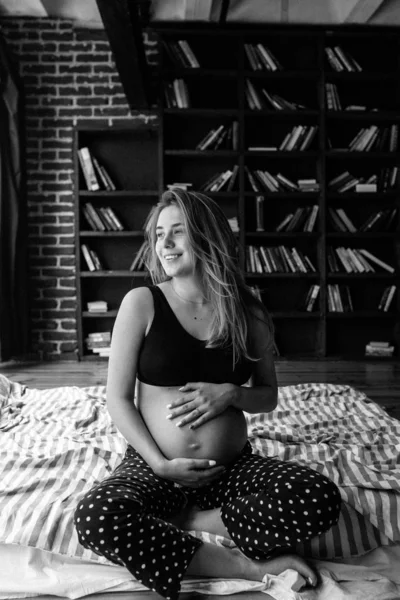 Attraente donna incinta è seduta a letto e tenendo la campana — Foto Stock