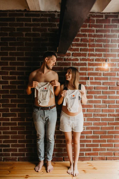 Pais grávidas segurando roupas de bebê bonito — Fotografia de Stock