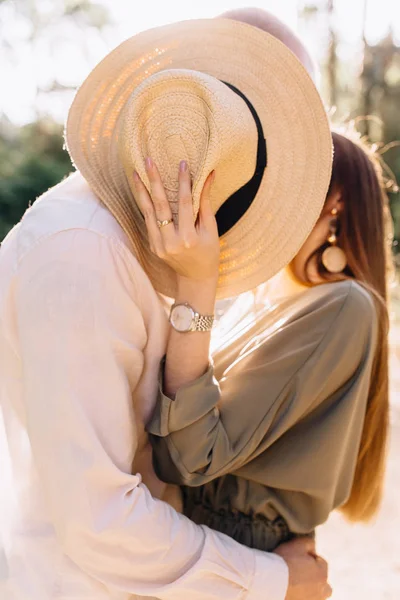 Para całująca się zakrywająca twarze słomkowym kapeluszem. Miłość w ol — Zdjęcie stockowe