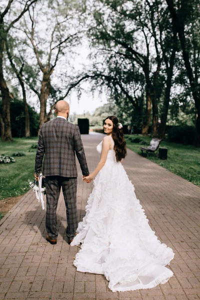 Uma noiva bonita fica de costas em seu vestido de noiva. Vestido com renda. A noiva feliz está girando — Fotografia de Stock