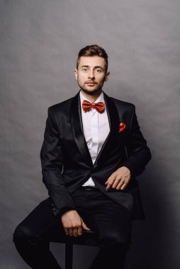 Siyah takım elbiseli, beyaz gömlekli, bar taburesinde oturan esmer bir adam.