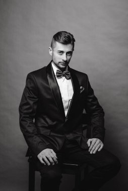 Siyah takım elbiseli, beyaz gömlekli, bar taburesinde oturan esmer bir adam.