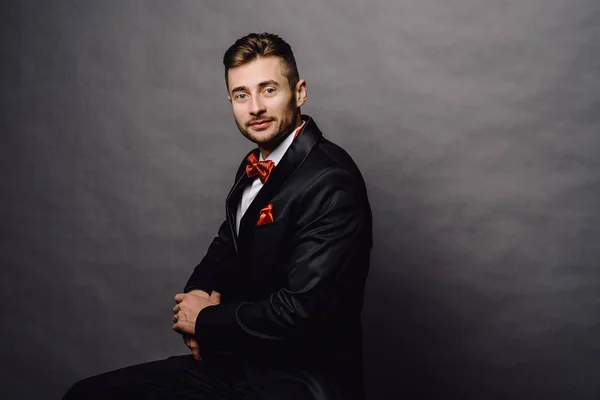 Серьезный бизнесмен в элегантном двубортном костюме сидит на стуле на сером фоне студии — стоковое фото
