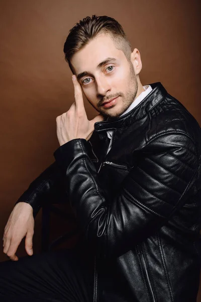 Handsome young man isolated. Fashionable man in leather jacket is standing on brown background.