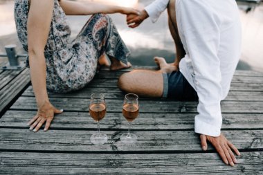 Romantik kırmızı şarap ile pier üzerine oturan Çift.