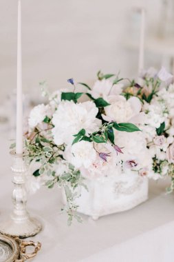 Düğün ziyafeti masası. Tabaklar, bardaklar, çatal bıçak takımı ve çiçek aranjmanı beyaz yuvarlak bir masada. Yuvarlak masa, beyaz bir masa örtüsü. Gri bir peçeteyle kaplanmış bir tabak..