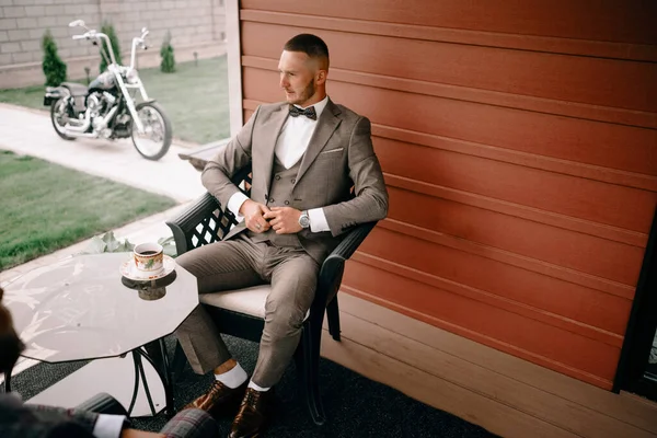 Young calm man relaxing sitting on terrace chair hands behind head, relaxed guy breathing fresh air, meditating with eyes closed outside modern house, resting alone, enjoying pleasant morning outdoor