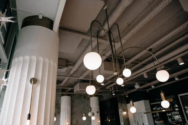 Gri tuğlalı duvarları, beton zemini, sandalyeli kare masaları ve tabureli barları olan çatı katı tarzı bir restoran..