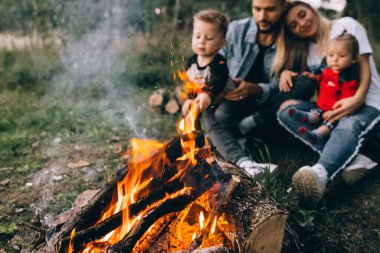 Kovboy şapkalı insanlar kamp ateşinin yanında konuşuyor.