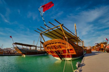 Katara plajında geleneksel ahşap kayıklar (dhows) Katar bayrağı ve gökyüzünde bulutlar olan Katar gündüz görüşü