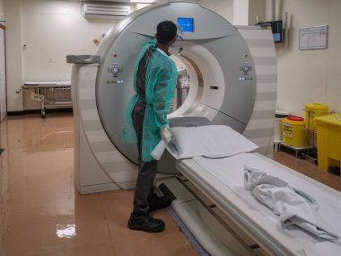 Radyoloji Bölümü 'nde kişisel koruyucu ekipman (PPE) giyen radyoloji teknisyeninin Corona virüsü hastasını (COVID-19) inceledikten sonra dezenfekte ettiği hesaplanmış tomografi makinesi (CT))