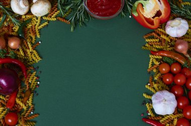 Tortiglioni üç renkli çiğ makarna, sebze ve baharatlar, koyu yeşil arka planda domates sosu. Yukarıdan bak. Yemek pişirme konsepti.