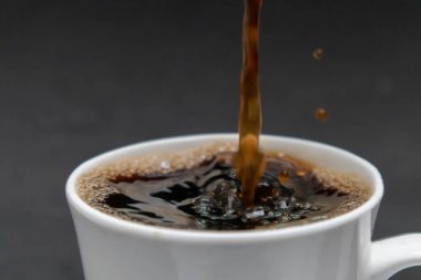 Sıcak kahveyi beyaz bir fincana dolduruyor. Taze kahve, siyah arka plan.