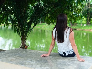 Üzgün ve depresif genç bir kadın. Parktaki beton bir bankta oturmuş göle bakıyor. Üzgün, yorgun ve yalnız hissediyor. Boşluğu kopyala