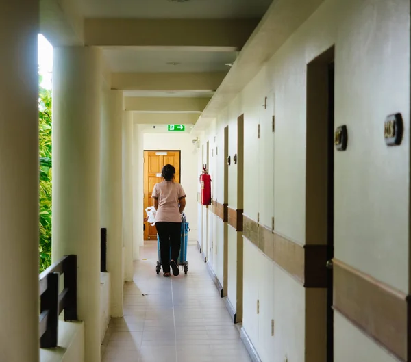 The hotel staff, a girl in uniform, rolls a cart with supplies down a long corridor