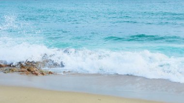 Dalgalar, turkuvaz renginde, kıyıdaki kayalıklarda köpük ve sprey ile sıçrayıp kırılıyor.