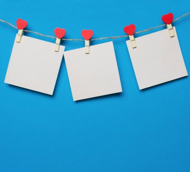 Kağıtlar ahşap raptiyelerde asılı, mavi arka planda kırmızı kalpler sevgililer gününde sevdiklerine selam yazmak için.