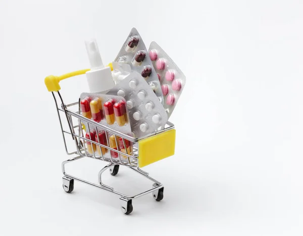 Beyaz arka planda, bir tüketici arabasında soğuk algınlığı, grip ve viral hastalıklar için ilaçlar. Alışveriş arabasında haplar, vitaminler ve burun spreyi..