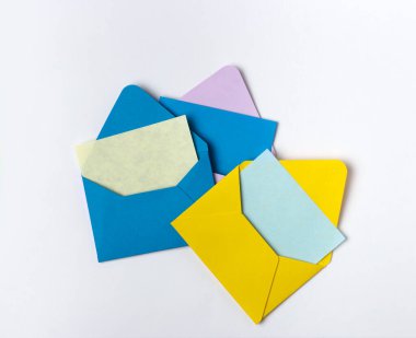 Davetiye için renkli zarflardan üçü, açık gri arka planda ve boş kartla. Minimalist biçimli kompozisyon, üst görünüm