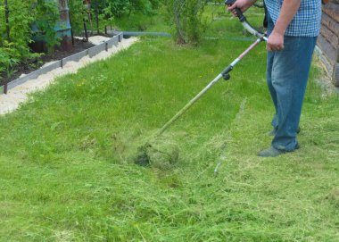 Bir bahçıvan arka bahçedeki çimleri benzin makası ile biçiyor.