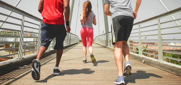 people jogging on sunny day wearing sportswear on an urban bridge view from behind.