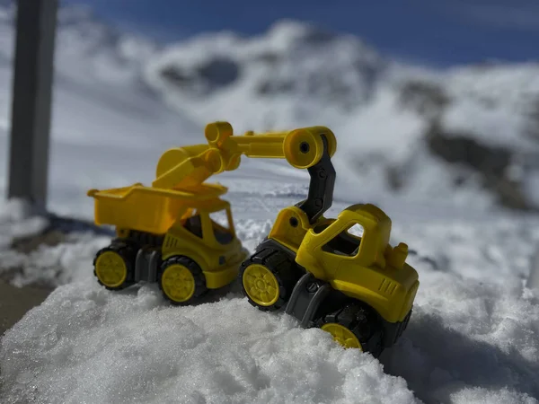 Toy trucks and excavators in the snow in front of a snowy mountain in the Swiss Alps on a sunny winter day