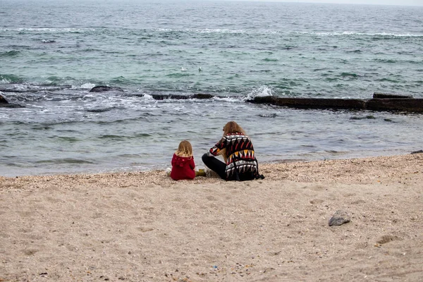 Menina com sua mãe na areia pela água no outono no mar — Fotografia de Stock