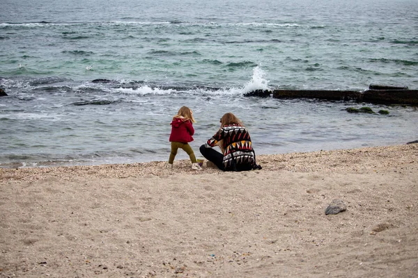 Menina com sua mãe na areia pela água no outono no mar — Fotografia de Stock