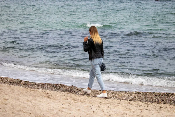 Блондинка в черной кожаной куртке осенью ходит по пляжу — стоковое фото
