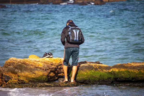 Um homem com uma mochila fica chutado na água no mar no outono — Fotografia de Stock