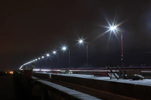 A row of street lamps at night on a bridge under construction