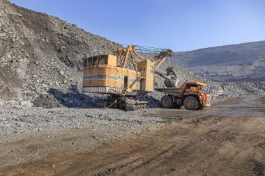 Taş ocağında büyük bir kazıcı büyük bir maden kamyonu yüklüyor.