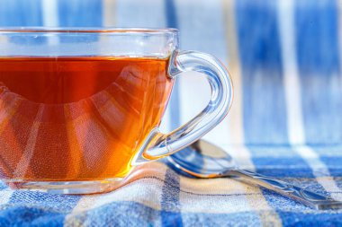 Damalı bir masa örtüsünde şeffaf bir fincanda siyah çay.