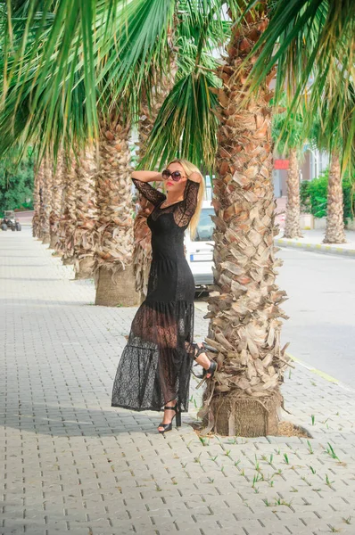 Blonde in a black  dress on the street with palm trees