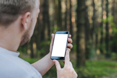 Adam ormanın arka planında elinde akıllı bir telefon tutuyor..