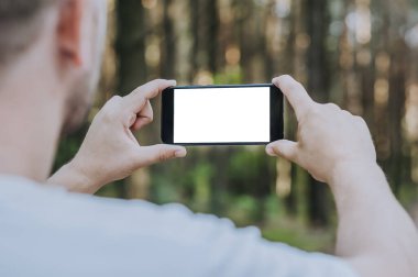 Adam ormanın arka planında elinde akıllı bir telefon tutuyor.