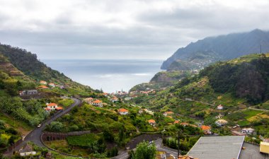 Koyu bulutlar, yüksek dağlar ve dik uçurumlarla kaplı bir sahil şeridi olan Madeiras 'ın kuzey kıyısındaki dramativ sahnesi. Öndeki yeşil tarlalarda ve Sao Jorge 'nin küçük köyünde. Büyük dalgalı mavi deniz.
