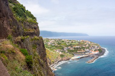 Kayalıklardan Portekiz, Madeira 'nın kuzey kıyısındaki küçük Ponta Delgada şehrine kadar. Adanın bir burnu üzerinde uzanmış denizi işaret eden, etrafını saran yüksek dağlarla tipik medreseli köyler ve evler..