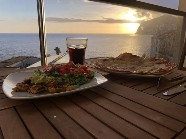 Food and drinks in front of a sunset view of cabo girao on madeira south coast. After a long day relaxing on the balcony with this perfect view of the sunset and sea, the sun vanishing behind cabo girao.