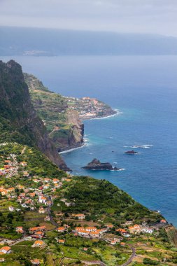 Kayalıklardan Portekiz, Madeira 'nın kuzey kıyısındaki küçük Ponta Delgada şehrine kadar. Adanın bir burnu üzerinde uzanmış denizi işaret eden, etrafını saran yüksek dağlarla tipik medreseli köyler ve evler..