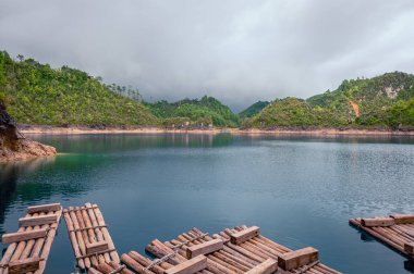 Turkuaz gölün kıyısında ahşap sallar, arka plan dağları ve bulutlu gökyüzü