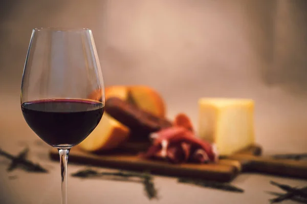Glass of red wine and in the background different gourmet cheeses, salami and bread on a wooden board
