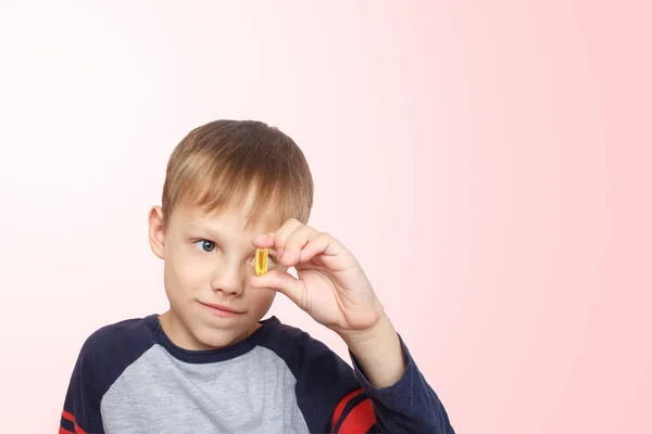 Küçük çocuk balık yağı alır. D vitamini, E. Parmaklarının arasında omega-3 kapsülü tutan çocuk. Sağlıklı beslenme. Boşluğu kopyala.