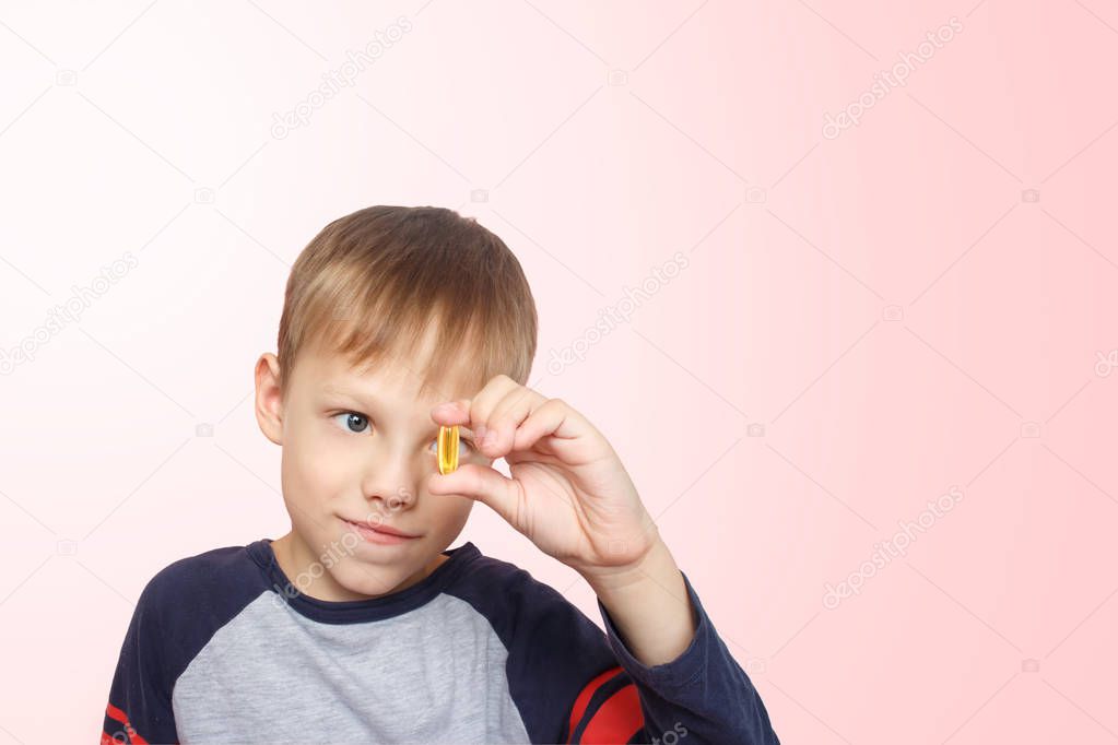 Little boy takes fish oil. Vitamins D, E. The child holding omega-3 capsule between his fingers. Healthy nutrition. Copy spase.