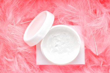 Beyaz konteynır krem kavanozu ve pembe tüyler üst görünüm bileşimi. Yaratıcı asgari güzellik düzleşimi.