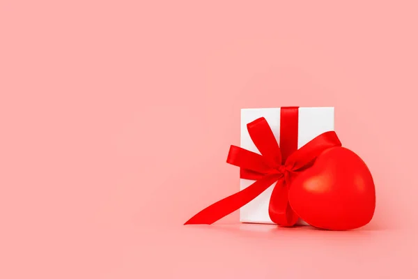 Szablon Szczęśliwego Dnia Kobiet. Dekoracyjne białe pudełko z czerwonym kokardą na pastelowym różowym tle. — Zdjęcie stockowe