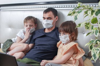 Sevimli çocuklar, kız ve erkek çocukları ve tıbbi maskeli babaları evde karantinada oturuyorlar. Evde kalma çağrısı salgını durdurur. Kendini izole etmek bir çözüm. Dikkat et Coperid-19.