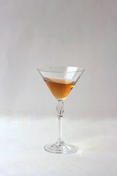 Gri zemin üzerinde sarı bir içecek bulunan martini bardağı. Yakın plan.
