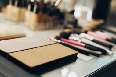 Masanın üzerinde ayna, fırça, ruj, krem, rimel ve saç spreyi var.